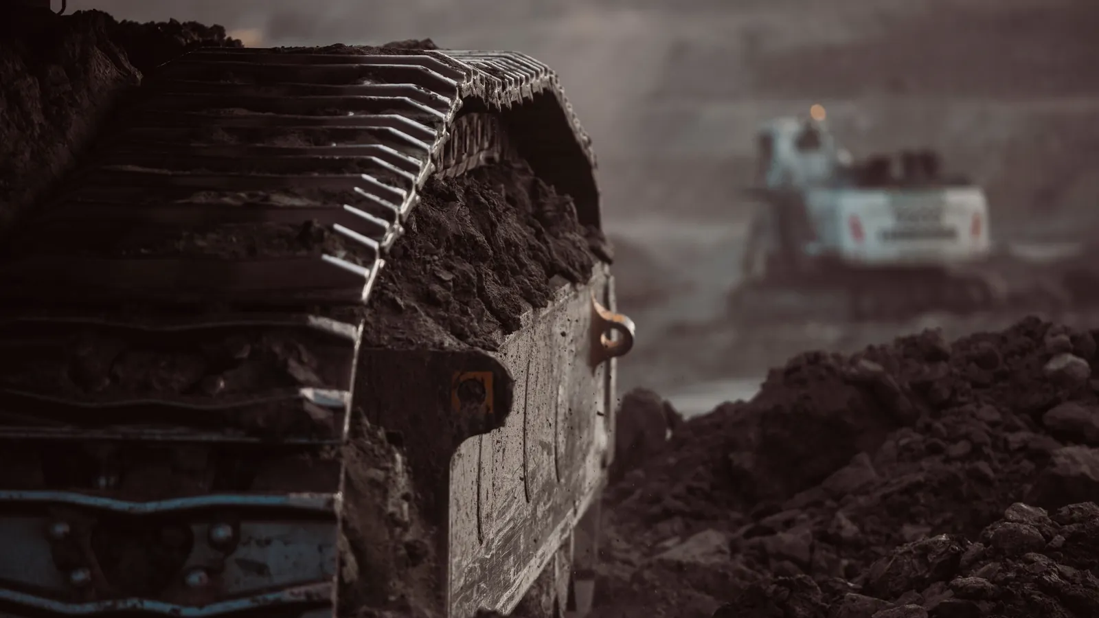 Close-up of a crawler track covered in earth on a mining site, an excavator in the background