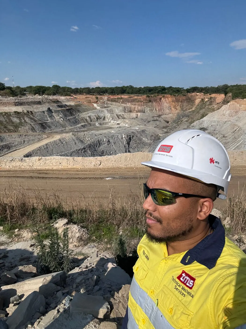 TMS field engineer in a TMS helmet and shirt overlooking an open pit mine